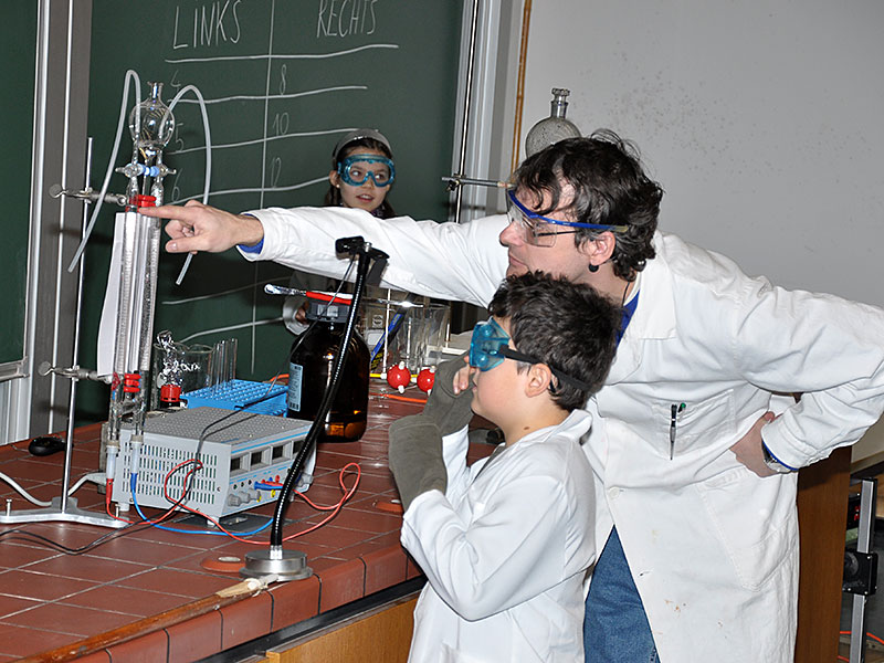 Wasser zerfällt in seine Bestandteile: Der Nachwuchsforscher liest mit Unterstützung von Wolfgang Kroutil ab, wie viel Wasserstoff und Sauerstoff sich bilden, seine junge Kollegin notiert die Werte an der Tafel. 
