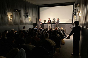 Bild von Kinosaal mit drei Personen im Gespräch vor der Leinwand 